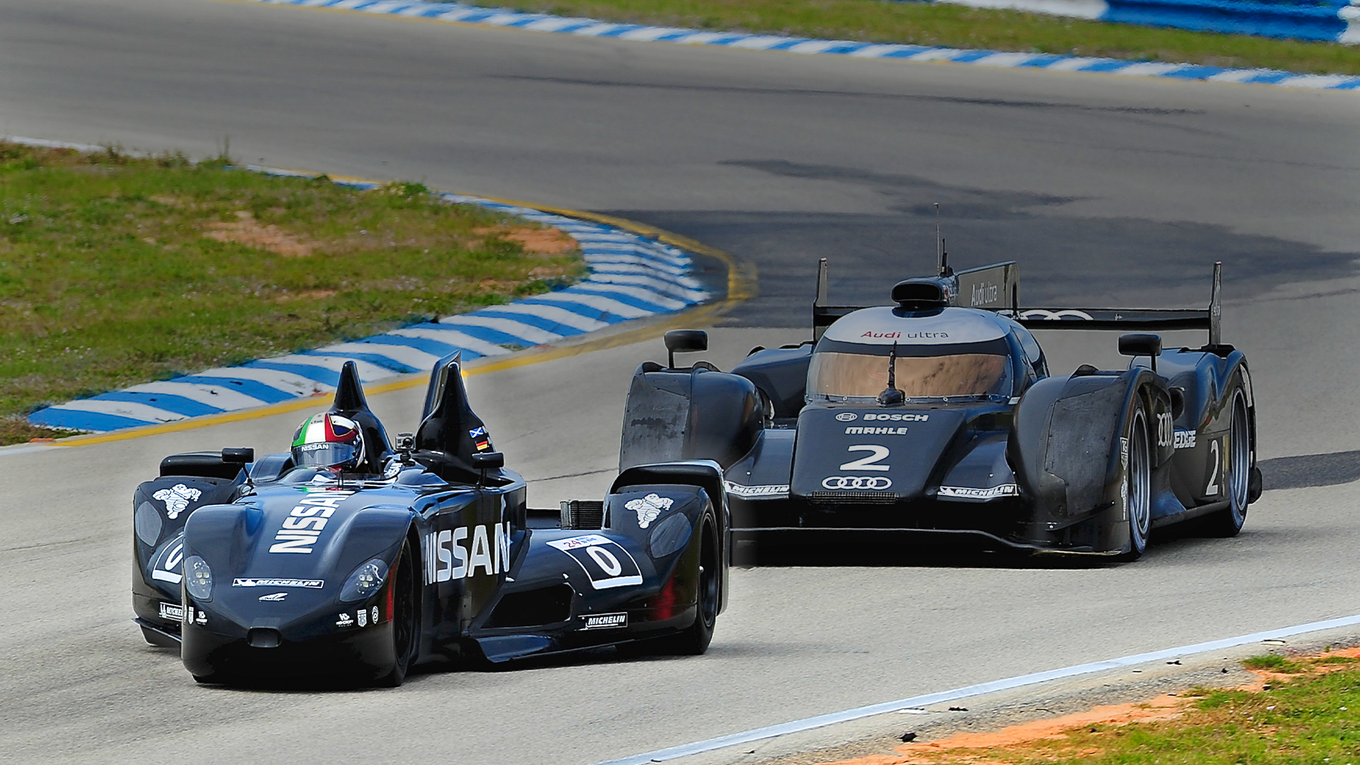 DeltaWing racecar on track with typical prototype car behind