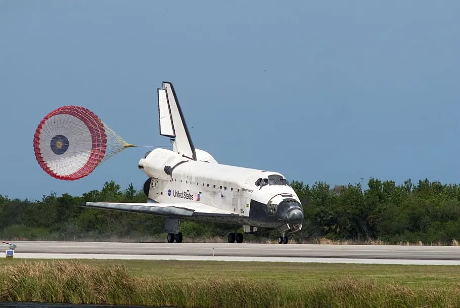 The Space Shuttle landing on a runway with parachute deployed